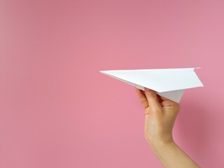Hand holding white paper airplane. Pink background. Paper airplane in hand close-up