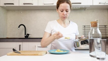 Woman putting pasta from a pot onto a plate, preparation of an Italian meal, culinary moment in a modern kitchen. - Powered by Adobe