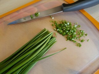 Bunch of green onions on a cutting board. Cutting board with sliced ​​onions and kitchen knife on table