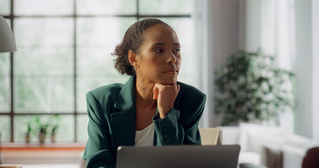 Portrait of Beautiful Black Woman Working on Laptop at a Sunlit Desk. Surrounded by Plants and Large Windows, She Focuses on Digital Design, Social Media Marketing Campaign. Medium Portrait