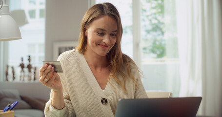 Young Attractive Woman Using Laptop Computer For Paying for Shopping or Service with a Credit Card on the Internet. Female Sitting in a Modern Cozy Office. Purchasing Cool Stuff Online Securely.