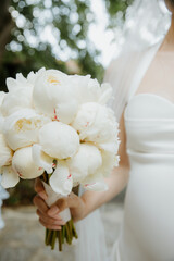 Bride Holding a White Peony Bouquet in Elegant Wedding Dress Outdoors
