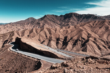 Winding road meandering through the Atlas Mountains of Morocco on a sunny day, with cars cruising along the scenic route