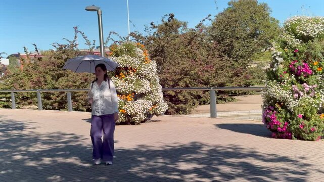 Woman walking with parasol in Juan Carlos I park in Malaga