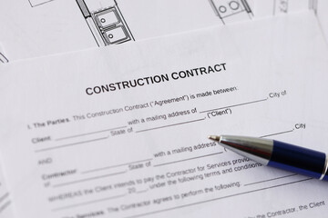 Pen on residential construction agreement and planning blueprints of residential building project...