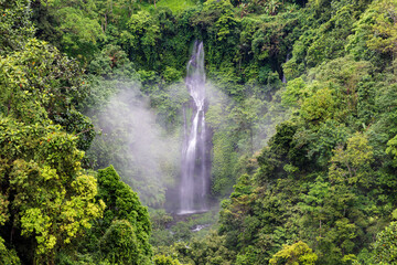 One of many waterfalls at Sekumpul waterfall, northern Bali, Indonesia. Mist rising from the water; surrounded by lush green cliffs.
