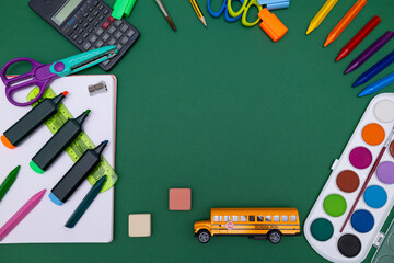 Colorful school supplies on green background of a blackboard