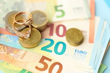European union Euro money bills and coins with wedding rings on blue table