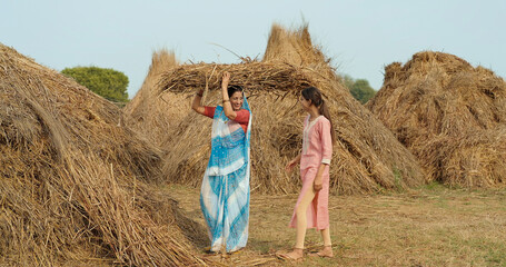 Indian young adult villager woman lady wear saree standing collecting dry grass outdoor Asian happy...