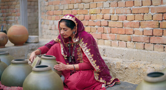 Indian village woman wear traditional saree sitting outdoor make hand made potters finishing touches clay pots asian gen x female learn handcraft create sculptor pottery mud product outside
