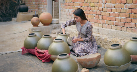 Indian teenage village woman wear casual dress sitting outdoor making hand made potters finishing...