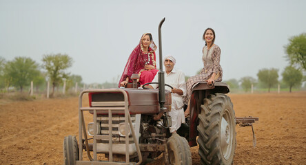 Obraz premium Indian village farmer young woman lady wear red saree smiling sitting on tractor outdoor Asian mother with teen age girl talk gossip old aged male man driving outside farm rural area enjoy desi life