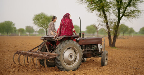 Obraz premium Indian village farmer young woman lady wear red saree smiling sitting on tractor outdoor Asian mother with teen age girl talk gossip old aged male man driving outside farm rural area enjoy desi life