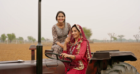 Indian village farmer mature woman lady wear red saree smiling sitting on tractor looking at camera...