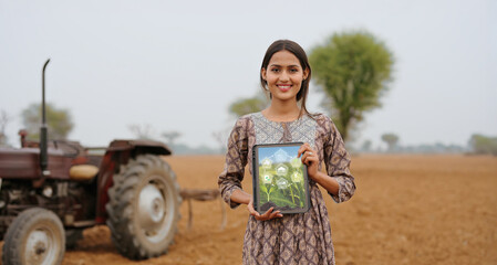 Indian young adult gen z farmer woman lady wear casual dress standing outdoor farmland hold green screen tablet device look at camera Asian smiling teen age girl do pose staring cam outside desi life
