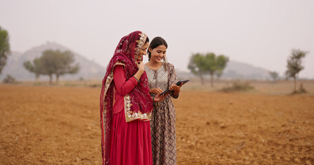 Indian asian villager farmer young adult woman lady wear red saree smiling outdoor hold tab device...