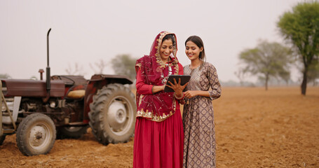 Indian asian villager farmer young adult woman lady wear red saree smiling outdoor hold tab device browse website data happy teen age girl teach mom talking enjoy day time outside desi life