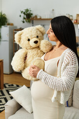 Beautiful young woman cradles teddy bear with love in bright modern living room while expecting baby