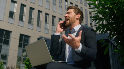 Stressed business man arguing mobile phone looking laptop throwing papers documents away in city Caucasian angry male businessman 40s employer middle-aged entrepreneur work job problem yelling mistake