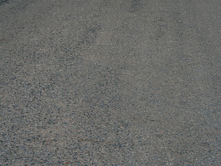 Detailed view of a textured asphalt road surface with visible aggregates and small pebbles. Natural lighting.