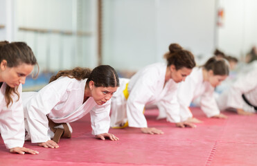 Group of female karatekas in kimono doing abdominal exercises in gym