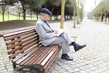 Obraz premium Senior professor writing notes while listening music on park bench