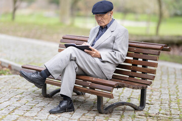 Fototapeta premium Elderly writer taking notes in notebook while sitting on park bench