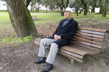Obraz premium Senior man relaxing on park bench listening music with earphones