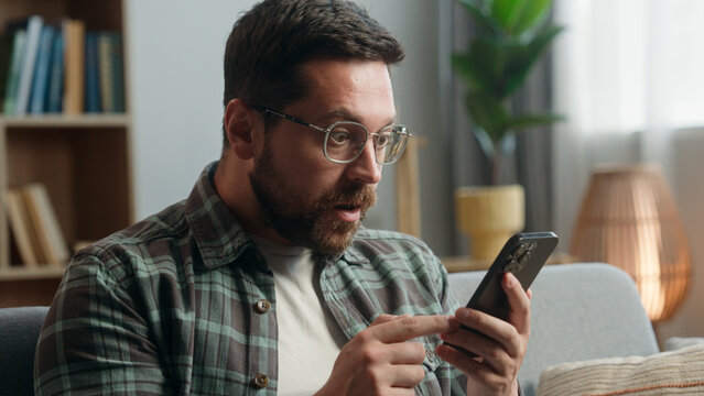 Portrait adult looking at mobile phone shock reaction amazed bad news close mouth with hand problem online indoors. Closeup male in apartment holding using smartphone shocked reaction at home scared
