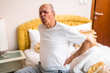 Obraz premium Senior man having pain in back after waking up and sitting on bed in the morning.