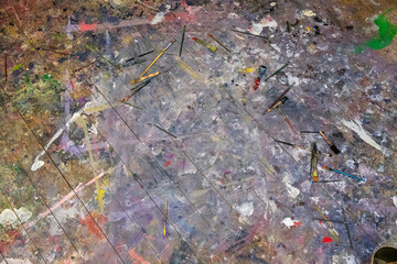 The floor surface, stained with paints and strewn with brushes, is a creative mess that reflects...