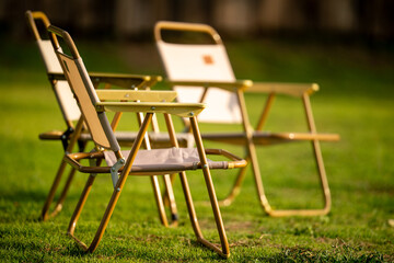 Two chairs are sitting on a grassy field. One of the chairs is a folding chair. The other chair is a folding chair with a white seat