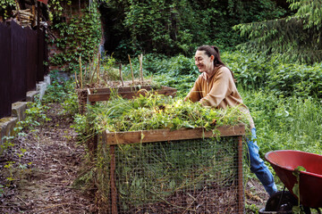 Woman adding garden waste and weeds to compost bin in backyard, sustainable gardening and organic...