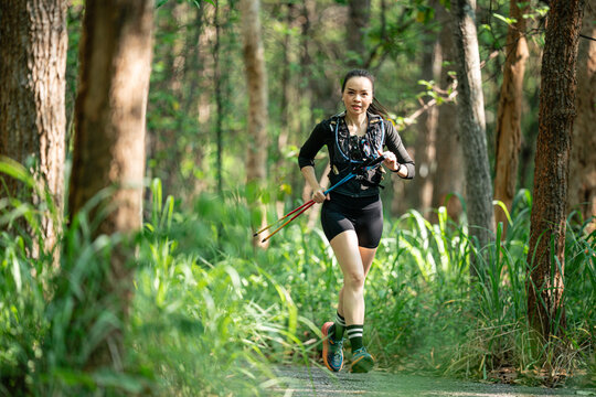 A woman is running through a forest with a pair of skis on. She is wearing a black outfit and has a backpack on her back - Powered by Adobe