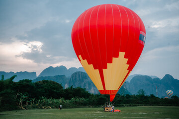 Obraz premium A red hot air balloon is sitting on the grass. There are two other hot air balloons in the background