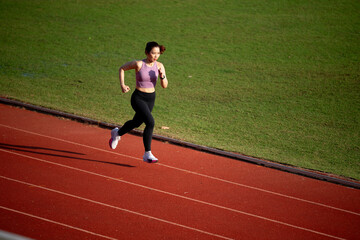 Fototapeta premium A woman running on a track. She is wearing a purple top and black pants. The track is red