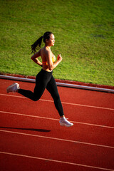 A woman running on a track. She is wearing a black top and black pants. She is wearing white shoes