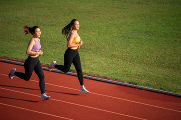 Two women running on a track. One is wearing a pink top and the other is wearing an orange top