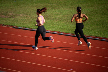 Obraz premium Two women running on a track. One is wearing a pink shirt. The other is wearing a black shirt