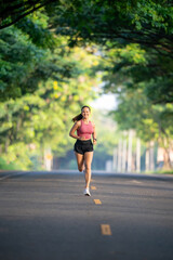 A woman is running on a road. She is wearing a pink shirt and black shorts. The road is empty