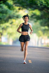 A woman is running on a road. She is wearing black shorts and a black tank top. She is wearing a watch and a wristband