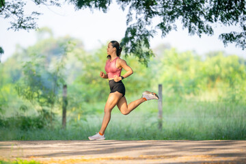 A woman is running on a road. She is wearing a pink shirt and black shorts. The road is surrounded by trees
