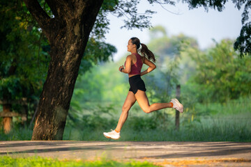 A woman is running in a park. She is wearing a red shirt and black shorts. The park is filled with trees and grass