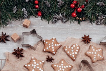 Christmas food flat lay. Tradition gingerbreads, cookie cutters, anise stars on baking paper and spruce decorative border.