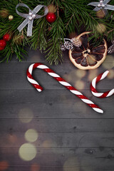 Christmas decorative upper border with green spruce, orange slice, cones, candy cane and holly berries on gray wooden background with bokeh, top view, copy space.