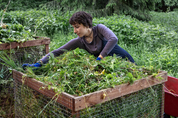Woman adding garden waste and weeds to compost bin in backyard, sustainable gardening and organic...