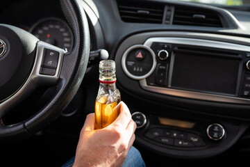 Driver driving a car with a bottle of alcohol in his hands close-up.
