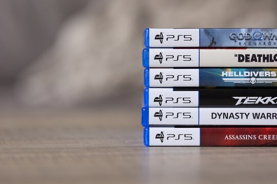 Brecht, Belgium - 18 april 2025: A stack of sony playstation 5 videogame cases or boxes lying on a wooden table. The pile of PS5 games are of multiple genres.