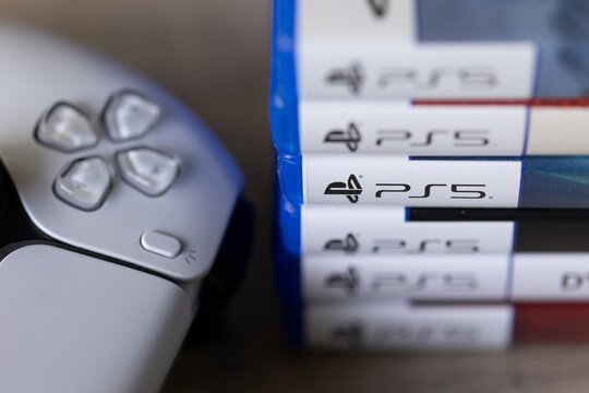 Brecht, Belgium - 18 april 2025: A close up portrait of a stack of sony playstation 5 videogame cases or boxes lying on a wooden table next to a PS5 wireless controller. Ready to play a console game.