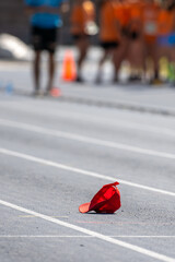 Red sports cap lying on the ground of a running track with blurred athletes in the background